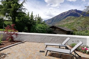 Eine Terrasse mit zwei Liegestühlen, einer Steinmauer und Blick auf die Berge.
