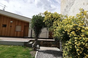 Ein modernes Gebäude mit Holzfassade, einer Steinsäule und einem Gartenbereich mit gelb blühenden Pflanzen.