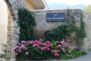 Eine Steinsäule mit einem Schild, auf dem 'BEIM NIEDERMOR' steht, und eine Gruppe pinkfarbener Blüten.