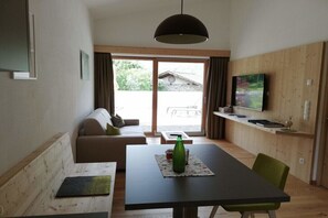 Een moderne woonkamer met een bank, een eettafel en een aan de muur bevestigde televisie.