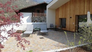 Un patio moderno al aire libre con piso de piedra, pared de madera y vistas a las montañas.