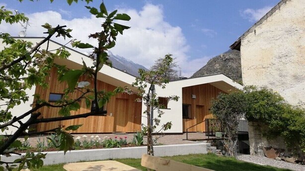 Un edificio moderno con fachada de madera, un pequeño jardín con flores y un cielo despejado.