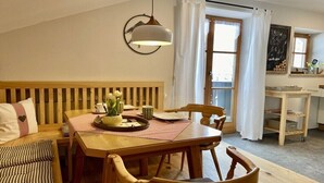 Ein gemütlicher Essbereich mit Holztisch, Stühlen und einer Bank. Über dem Tisch hängt eine Leuchte und es gibt ein Fenster mit Vorhängen.