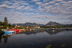 Ein ruhiger See mit Booten, eine Bergkette im Hintergrund und eine kleine Siedlung mit Häusern und einer Kirche.