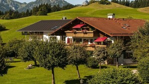 Ein Chalet mit geneigtem Dach, einem Balkon mit roten Markisen und Blick auf die Berge im Hintergrund.