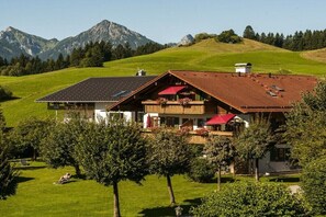 Een chalet met een schuin dak, een balkon met rode luifels en uitzicht op bergen.