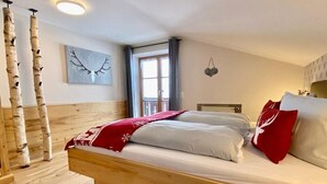 Ein Schlafzimmer mit einem hölzernen Bett, einem Fenster mit Vorhängen, einem an der Wand befestigten Kunstwerk und einem Holzboden.
