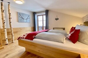 Een slaapkamer met een houten bed, een raam met gordijnen, een kunstwerk aan de muur en een houten vloer.