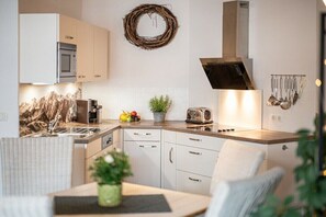 A modern kitchen with white cabinets, a stainless steel range hood, and a microwave. - Holiday apartment with 1 bedroom (Bolsterlang)