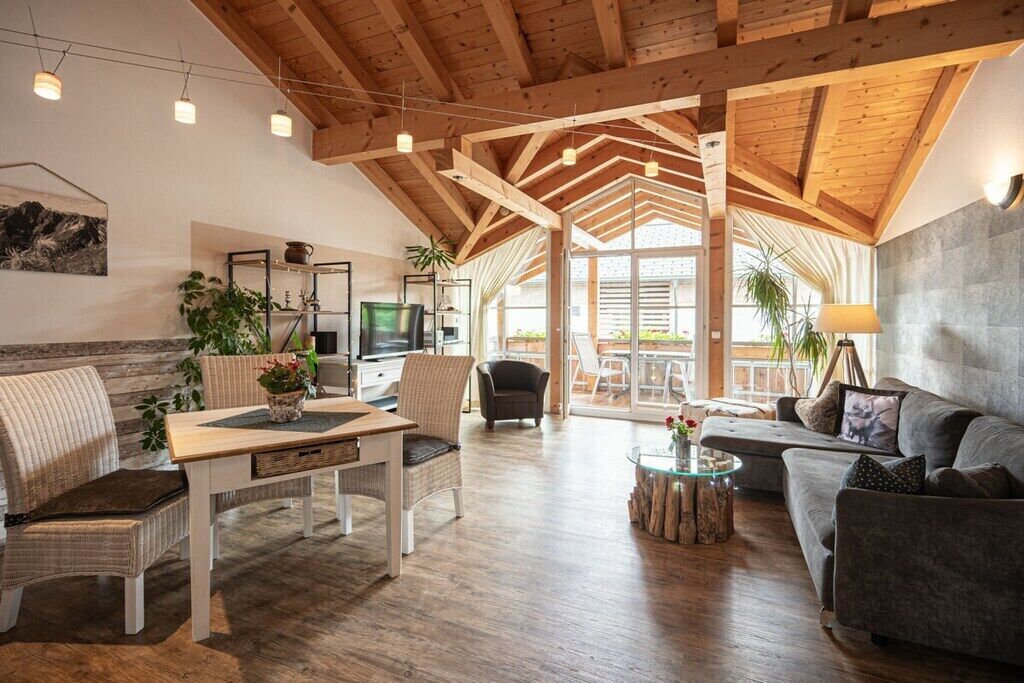 A spacious living area with a high ceiling, wooden beams, a television, and comfortable seating.