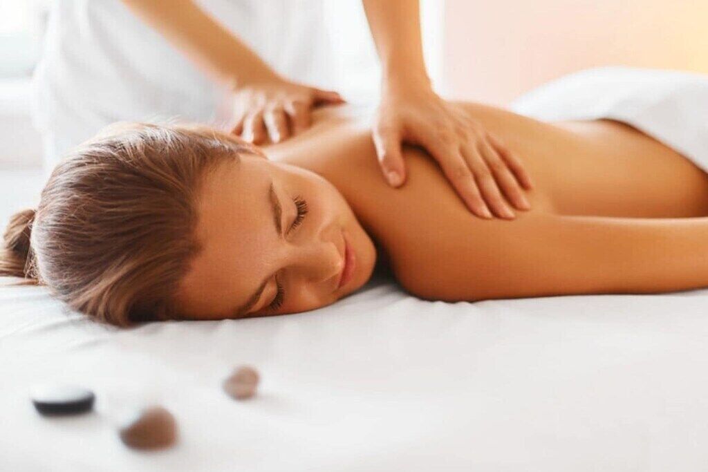 En person får en massage på ryggen medan hen ligger på en säng med ett vitt överdrag.