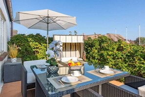 Ein Essbereich im Freien mit Tisch, Stühlen, Sonnenschirm und Obstkorb.