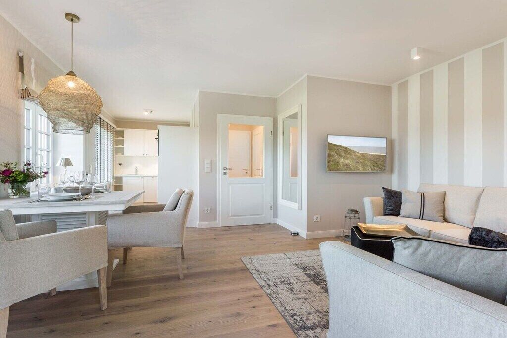 Una sala de estar moderna con un sofá, una zona de comedor con sillas y una cocina al fondo.