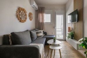 A modern living room with a grey sofa, a small round table, and a flat-screen TV mounted on the wall. - Riviera City Scape 1BR & Balcony. Athens (Glifada)