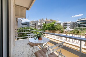 Un balcon avec une table et des chaises, un pot de fleurs et une vue sur les bâtiments environnants.