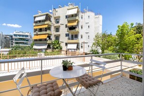 Un balcon avec une table et des chaises, un pot de fleurs et une vue sur un immeuble à plusieurs étages doté de balcons.