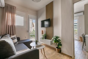 A modern living room with a sofa, a TV mounted on the wall, a small table, and a potted plant. - Riviera City Scape 1BR & Balcony. Athens (Glifada)