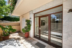 Une entrée d’immeuble avec une porte en verre, une plante en pot et un sol carrelé.