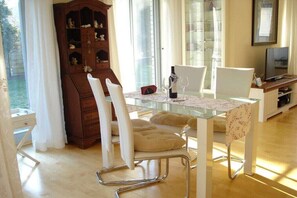 A dining area with a glass table, white chairs, and a wooden cabinet. - "Witt Hus" Home office and vacation (St-Peter Ording (Böhl))
