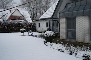 A residential area with snow-covered ground, a house with a brick facade, and a small garden with snow-covered bushes. - "Witt Hus" Home office and vacation (St-Peter Ording (Böhl))