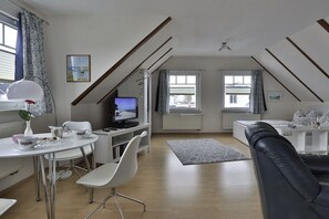 Una sala de estar moderna con televisor, muebles blancos y un sofá de cuero negro.