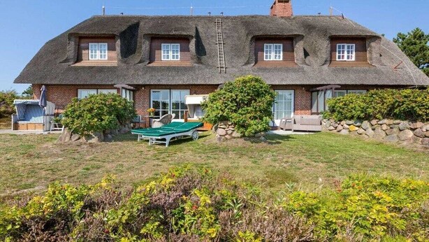 Ein zweistöckiges Haus mit einem Strohdach, ein kleiner Garten mit Rasenmäher und eine Steinmauer.