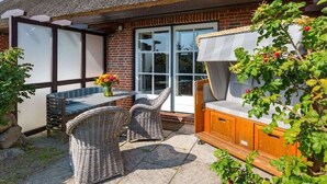 Eine Terrasse mit Korbmöbeln, einer Holzbank und einer Glastür zu einem Raum.