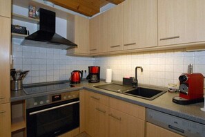 Una cocina con armarios de madera clara, una campana extractora negra, una cafetera roja, un fregadero y un lavavajillas.