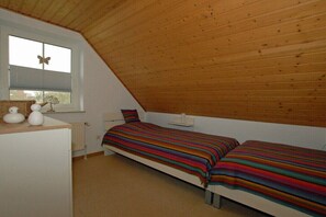 A small, single-room apartment with a sloped ceiling, a bed with a striped blanket, a dresser, and a window with a butterfly decoration. - Holiday home with 2 bedrooms (Wangerland-Hooksiel)