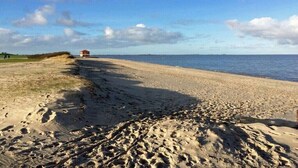 En sandstrand med fotspår som leder fram till en byggnad i fjärran.