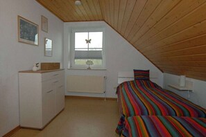 Un dormitorio con techo inclinado, una cama con ropa de cama a rayas, un aparador, una ventana con adorno de mariposa y un radiador.