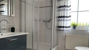 Ett modernt badrum med en dusch som är avskärmad med glasväggar, ett vitt handfat och en toalett.