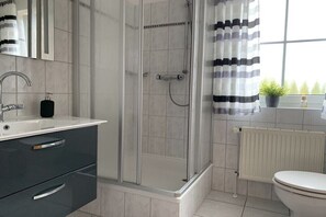 Un baño moderno con ducha envuelta en vidrio, un lavamanos blanco y un inodoro.