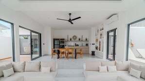 Een moderne woonkamer met een bank, een eethoek met een tafel en stoelen, en een keuken op de achtergrond.