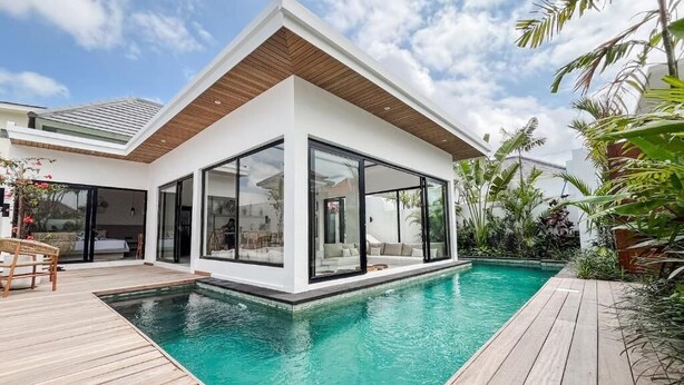 Een modern huis met een zwembad, grote glasramen en een houten terras.