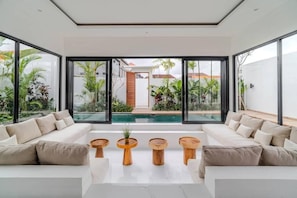 A modern living room with a large glass wall, a pool, and a sofa set. - Majys 3 Villa by Tasvan (Badung)