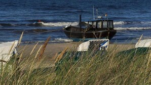 Um barco numa praia arenosa, com o oceano ao fundo.
