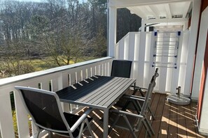 Een balkon met een tafel en stoelen, een witte leuning en uitzicht op bomen.