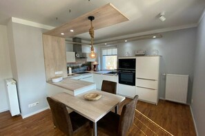 A modern kitchen with a central island, built-in appliances, and a dining area with a wooden table and chairs. - Holiday apartment with 1 bedroom (Bansin)
