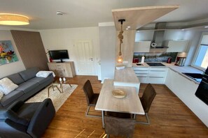 A modern living space with a dining area, a sofa, a television, and a kitchen in the background. - Holiday apartment with 1 bedroom (Bansin)