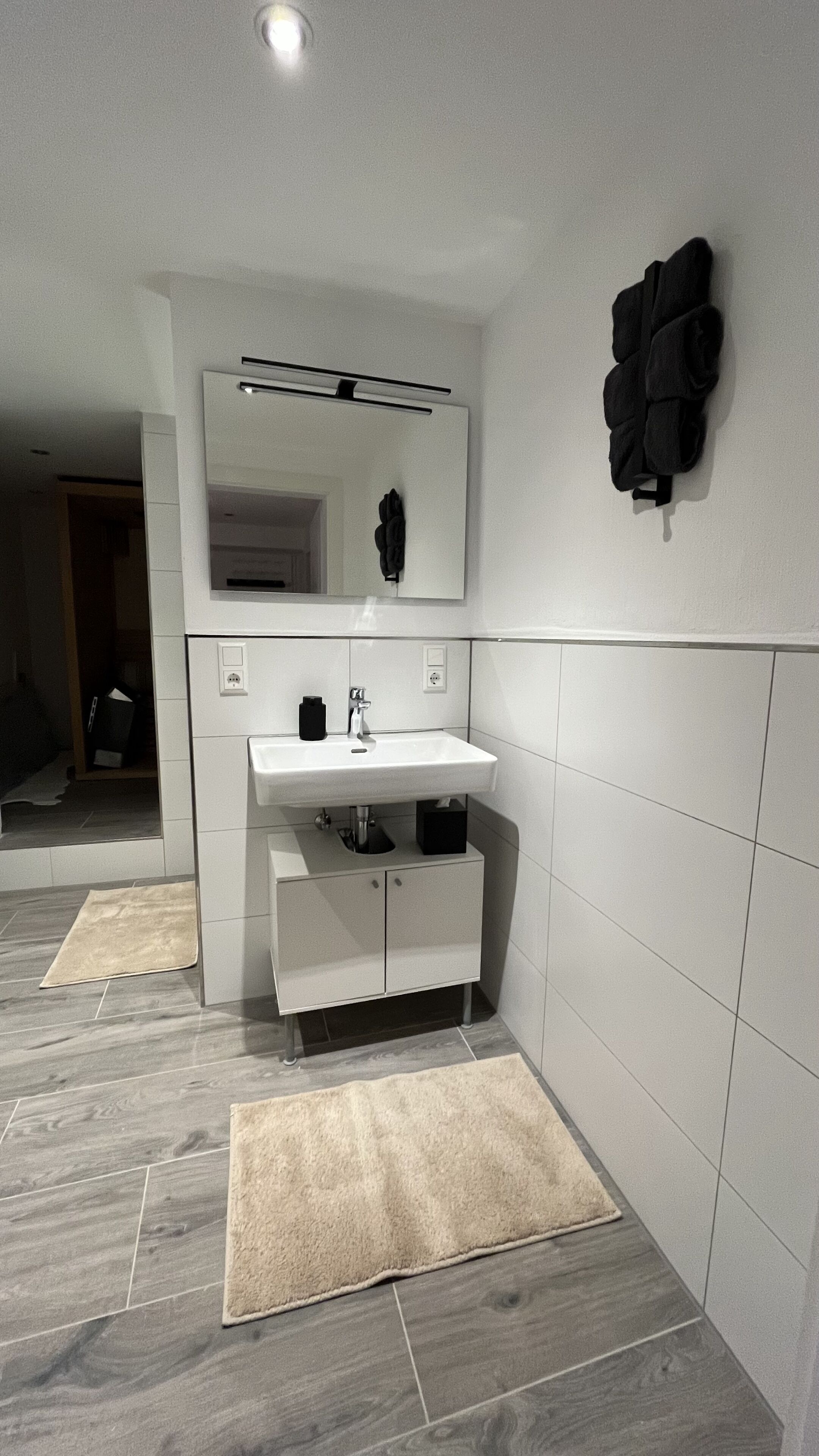 Een moderne badkamer met een wit wastafelmeubel, spiegel en een zwarte handdoekhouder.