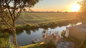A riverside deck with outdoor seating, a boat, and a view of a field and wind turbines. - Holiday home in Neufeld with swimming pool (Neufeld)