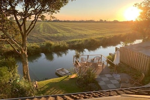 Una terrazza sul fiume con posti a sedere all'aperto, una barca e vista su un campo e turbine eoliche.