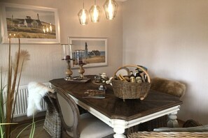 A dining table with a basket of bottles, a candle holder, and framed pictures on the wall. - Holiday home in Neufeld with swimming pool (Neufeld)