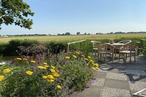 An outdoor seating area with a table and chairs, surrounded by a garden with various flowers and a view of a field. - Holiday home in Neufeld with swimming pool (Neufeld)