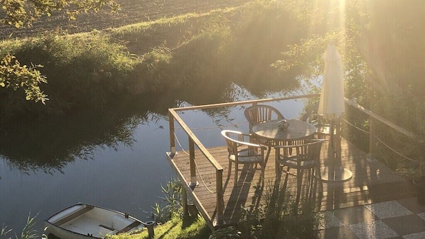 A wooden deck with a table and chairs overlooking a calm body of water, with a boat docked nearby. - Holiday home in Neufeld with swimming pool (Neufeld)