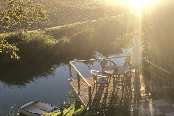 Un pontile di legno con tavolo e sedie che si affaccia su un'acqua calma, con una barca ormeggiata nelle vicinanze.