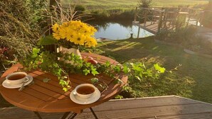A wooden table with two cups of tea and a vase of yellow flowers, overlooking a body of water and a grassy field. - Holiday home in Neufeld with swimming pool (Neufeld)