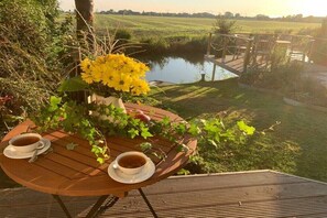 Un tavolo di legno con due tazze di tè e un vaso di fiori gialli, con vista su uno specchio d'acqua e un prato.