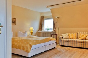 A bedroom with a bed, a sofa, a lamp, and a window. - House section Heideblick (Kampen)